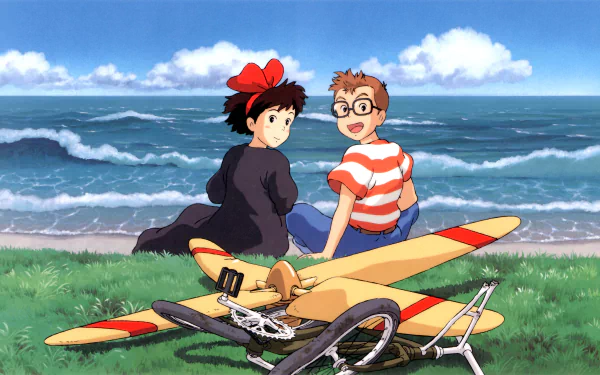 HD PC desktop wallpaper featuring anime characters Kiki and Tombo from Kiki's Delivery Service sitting by the ocean with a bicycle and colorful glider.
