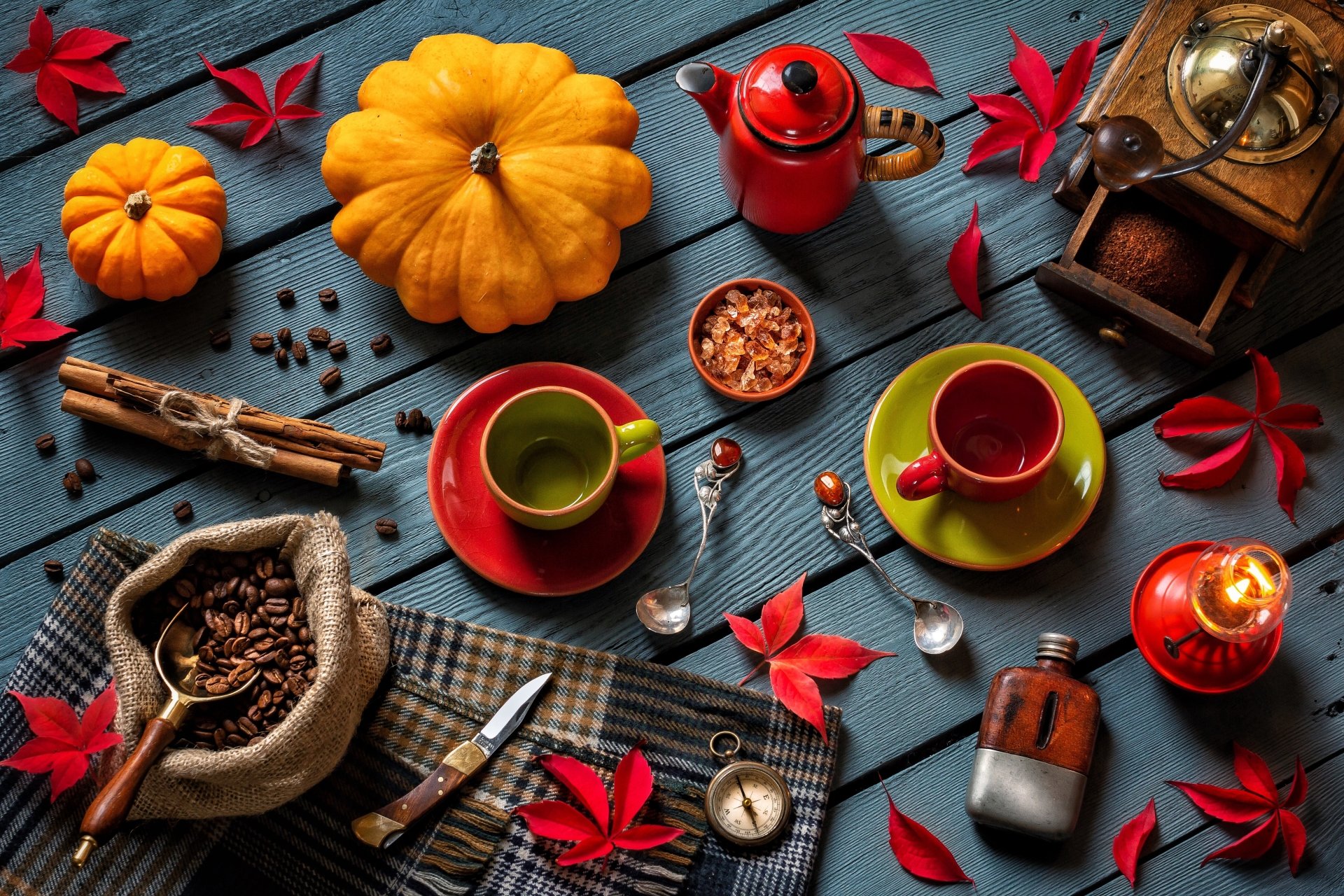 A vibrant still life featuring coffee beans, cinnamon sticks, a grinder, pumpkin, lantern, compass, spoon, knife, and colorful cups arranged on a dark wooden surface in 4K Ultra HD.