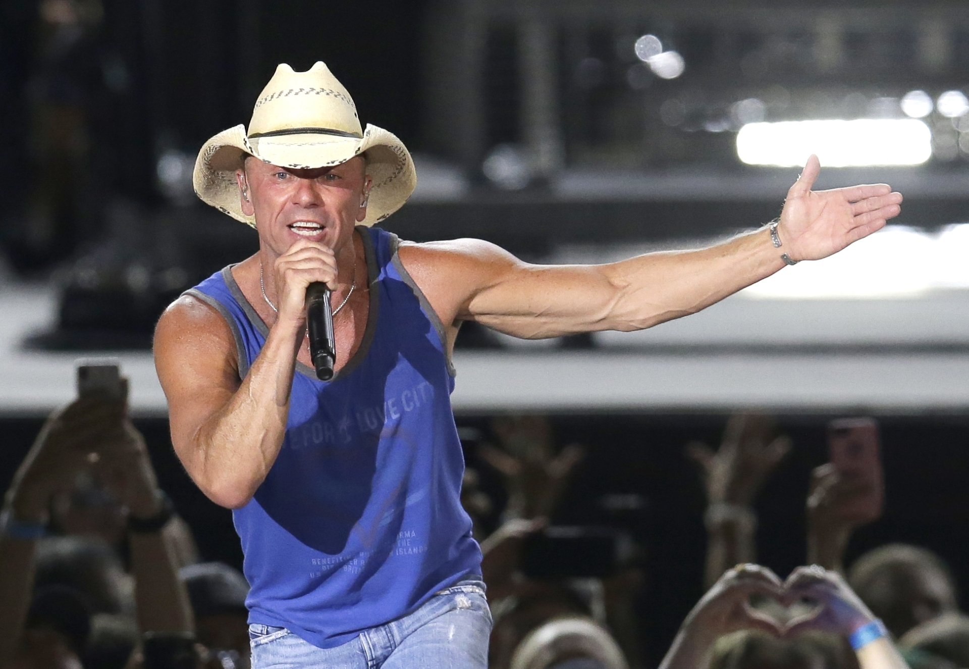 HD desktop wallpaper featuring a performer in a cowboy hat and blue sleeveless shirt singing on stage, tagged with Kenny Chesney.