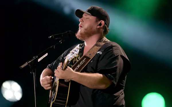 HD desktop wallpaper of a performer singing and playing guitar onstage with a blurred background of stage lights.