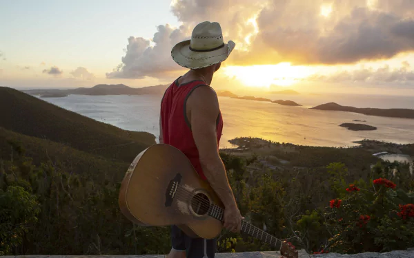 HD wallpaper featuring a person with a guitar looking at a sunset over a coastal landscape, tagged with Kenny Chesney.