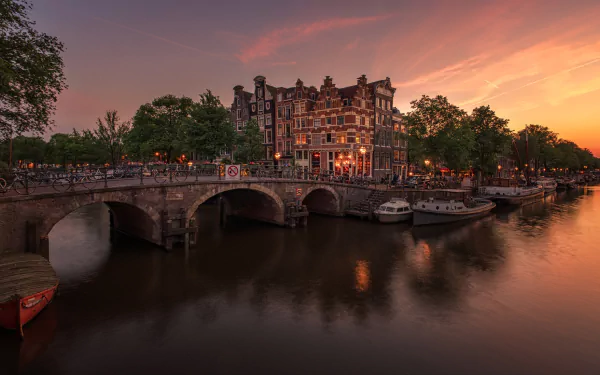 HD desktop wallpaper featuring a man-made canal scene in Amsterdam, Netherlands, with historic buildings and a sunset sky reflecting on calm waters.