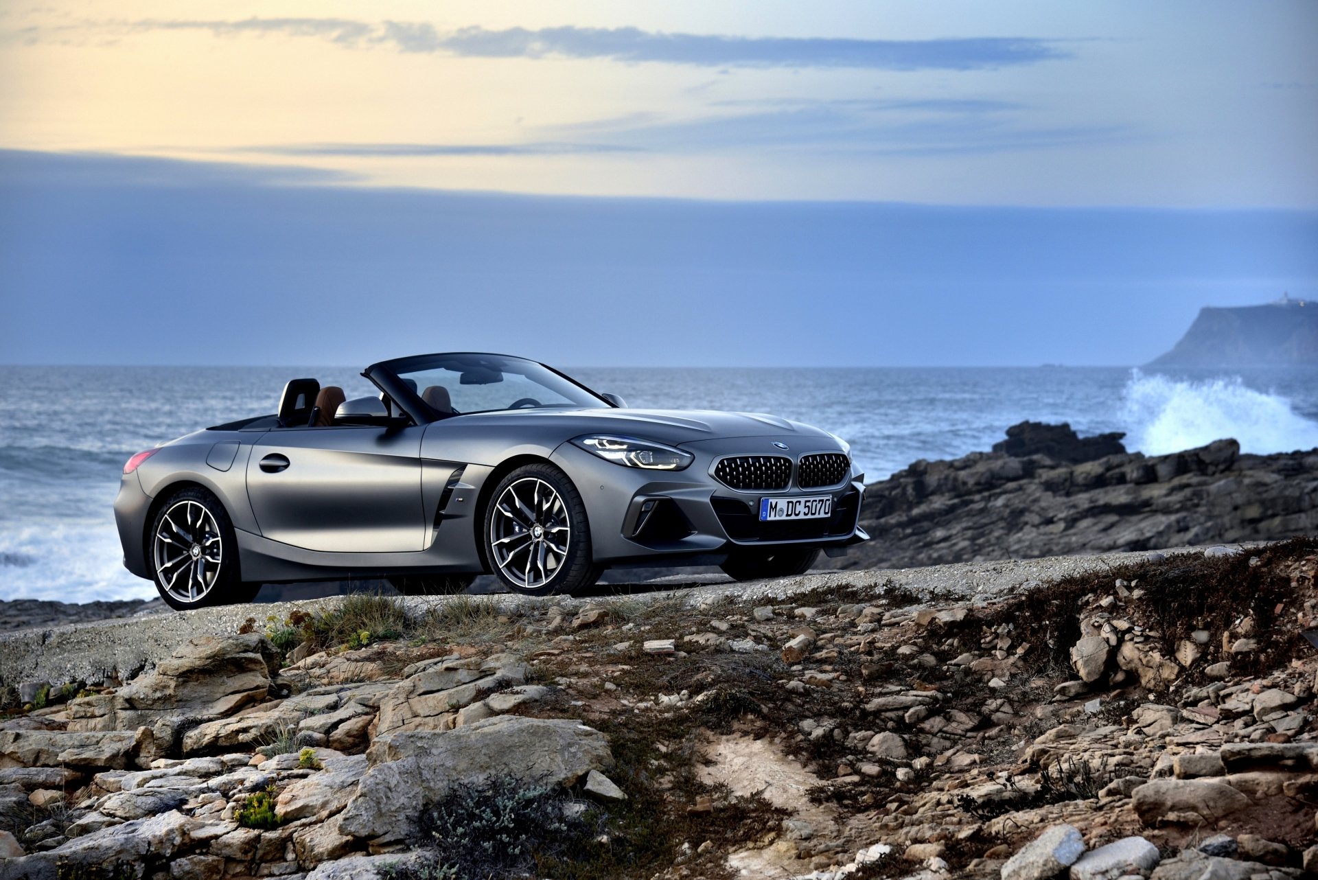 A silver BMW Z4 cabriolet parked on rocky terrain by the ocean under a cloudy sky, captured in stunning 4K Ultra HD as a desktop wallpaper background.