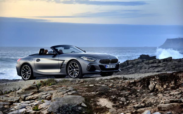 A silver BMW Z4 cabriolet parked on rocky terrain by the ocean under a cloudy sky, captured in stunning 4K Ultra HD as a desktop wallpaper background.