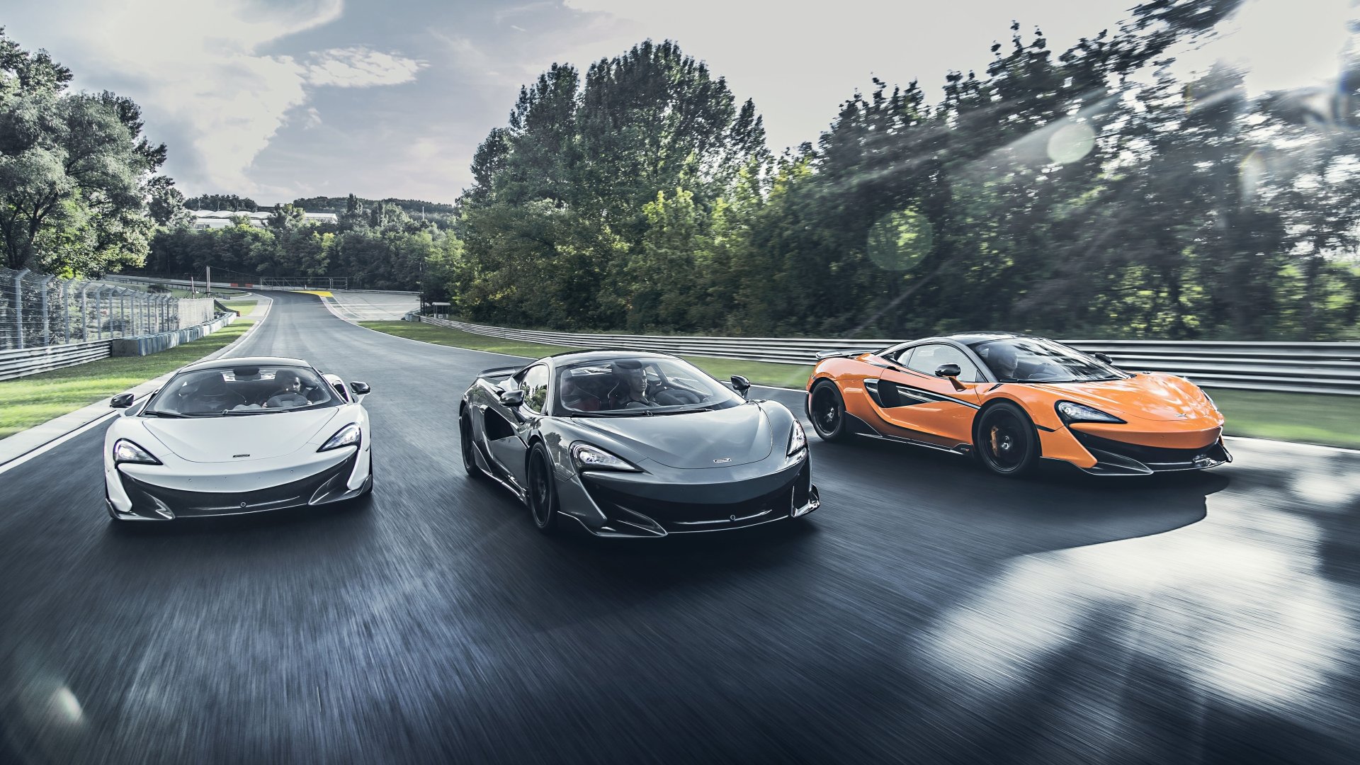 5K Ultra HD PC desktop wallpaper of three McLaren 600LT supercars — white, silver and orange — driving side-by-side on a tree-lined road.