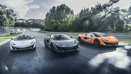 5K Ultra HD PC desktop wallpaper of three McLaren 600LT supercars — white, silver and orange — driving side-by-side on a tree-lined road.