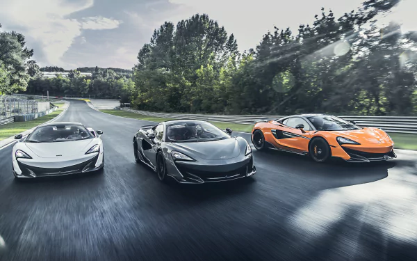 5K Ultra HD PC desktop wallpaper of three McLaren 600LT supercars — white, silver and orange — driving side-by-side on a tree-lined road.