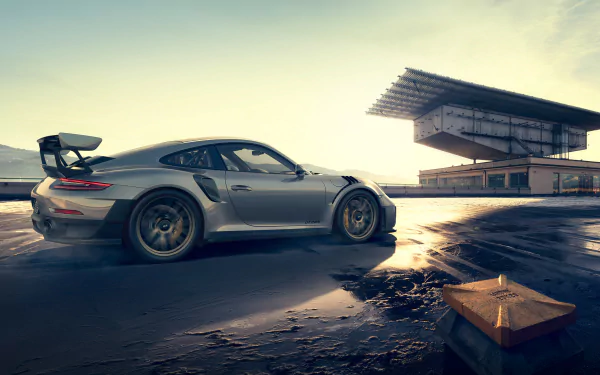 Silver Porsche 911 GT2 RS on a wet racetrack at sunset — dramatic 2K Quad HD PC desktop wallpaper showcasing the high-performance Porsche 911 GT2 sports car.