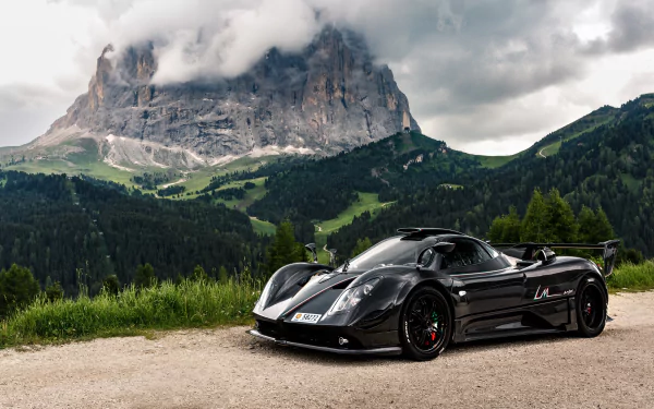 A sleek black Pagani Zonda supercar parked on a mountain road, set against a dramatic cloudy sky and lush green hills in this 4K Ultra HD desktop wallpaper.