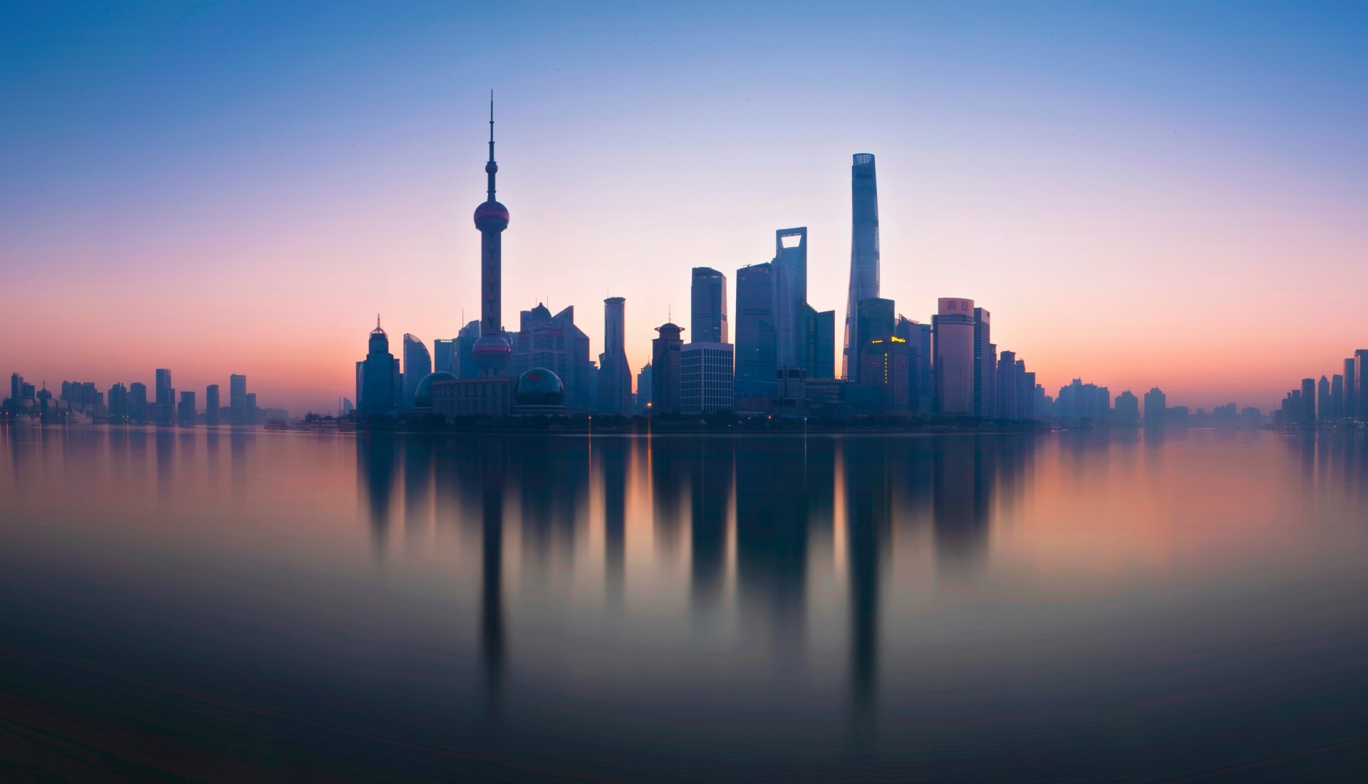 Panoramic 8K Ultra HD view of Shanghai’s iconic city skyline in China, showcasing modern man-made skyscrapers reflected on calm water at sunrise.