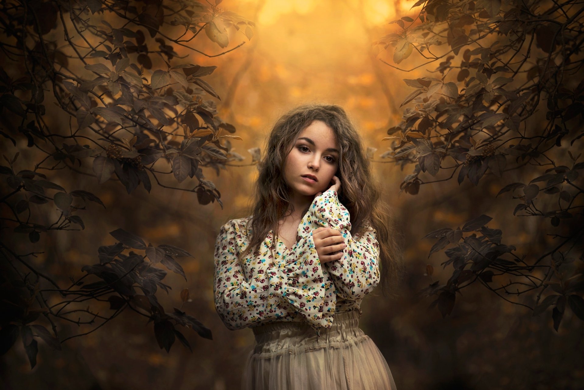 A brunette woman model stands pensively in a forest, bathed in golden light. HD desktop wallpaper and background. Mood: thoughtful, serene.