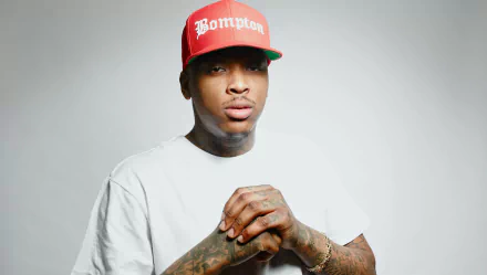 HD desktop wallpaper featuring YG in a white tee and red Bompton cap, posed against a grey backdrop.